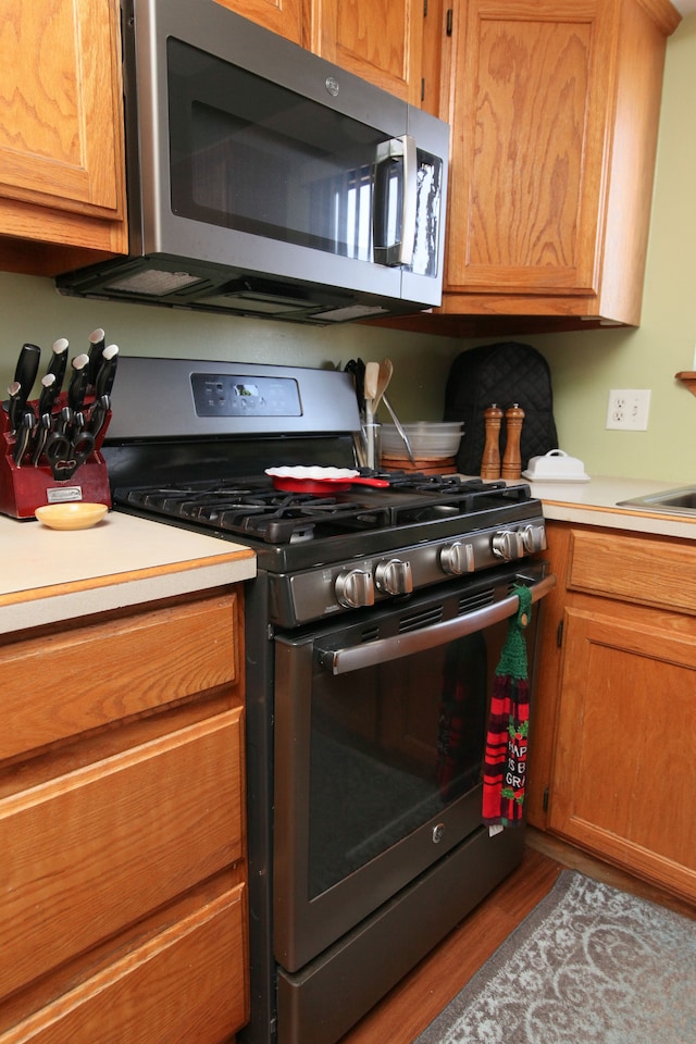 kitchen featuring brown cabinetry, appliances with stainless steel finishes, light countertops, and wood finished floors