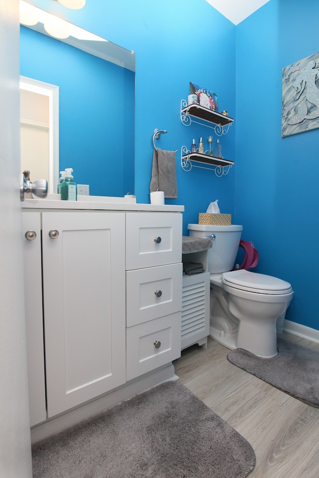 half bath featuring toilet, vanity, baseboards, and wood finished floors