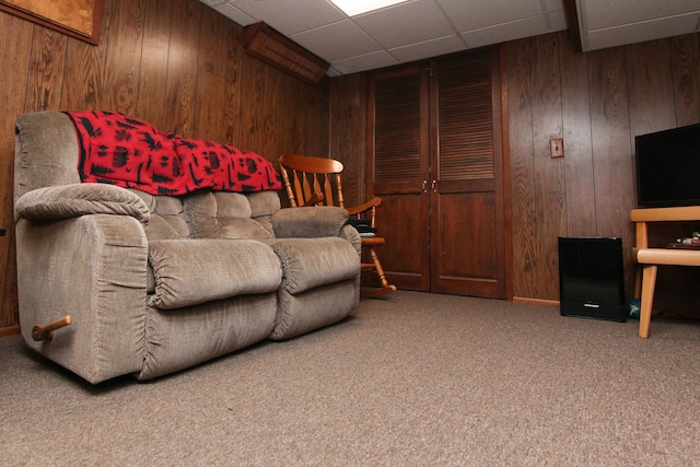 living area with a drop ceiling, carpet floors, and wood walls