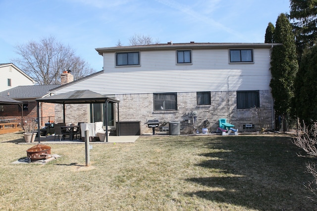 rear view of property featuring a gazebo, a fire pit, a patio area, a lawn, and brick siding