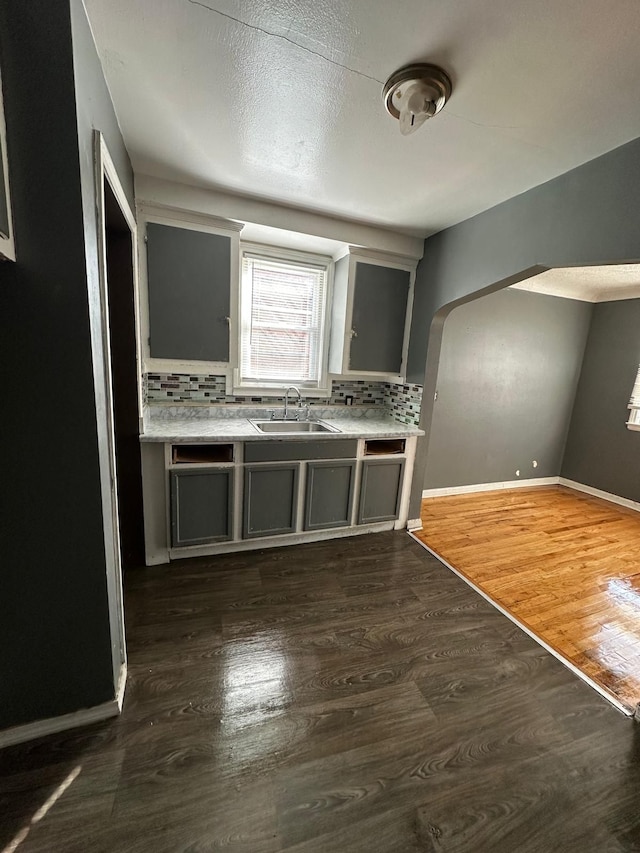 kitchen with arched walkways, dark wood-style flooring, tasteful backsplash, and a sink