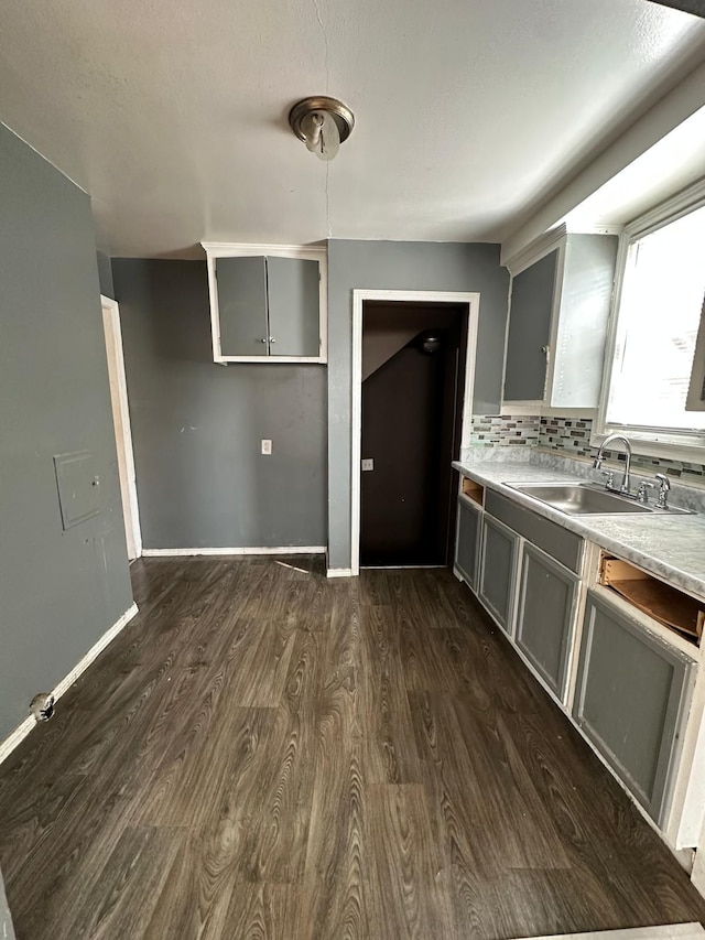 kitchen featuring dark wood-type flooring, gray cabinetry, backsplash, and a sink