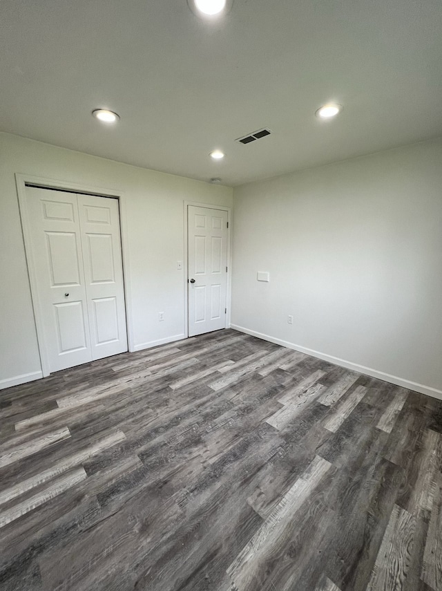 unfurnished bedroom featuring visible vents, baseboards, a closet, and dark wood-style flooring