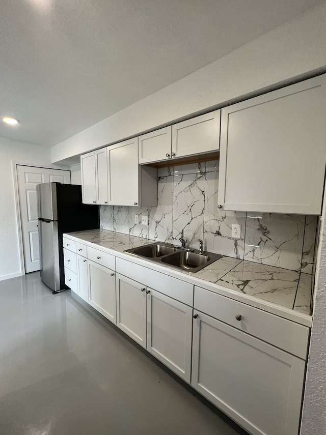 kitchen with a sink, tasteful backsplash, light countertops, and freestanding refrigerator