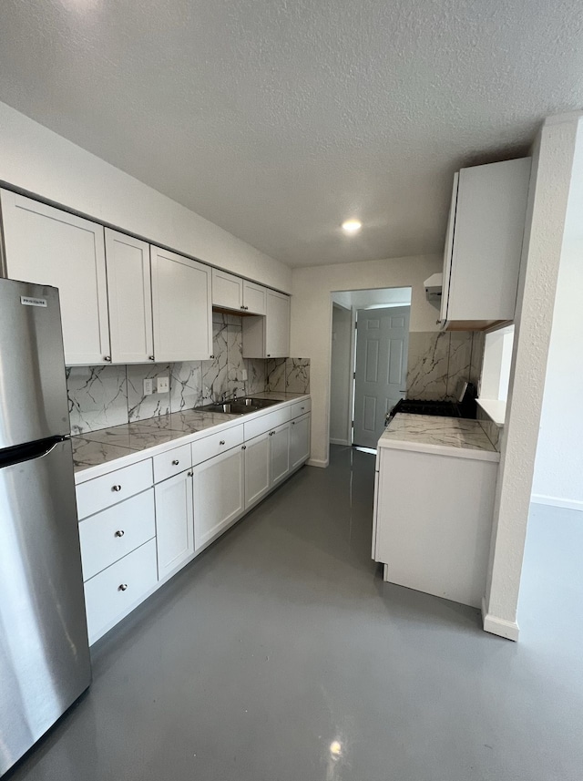 kitchen with backsplash, finished concrete floors, light countertops, and freestanding refrigerator