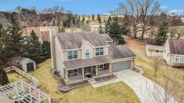 view of front of house with covered porch, a front lawn, concrete driveway, a storage unit, and a garage