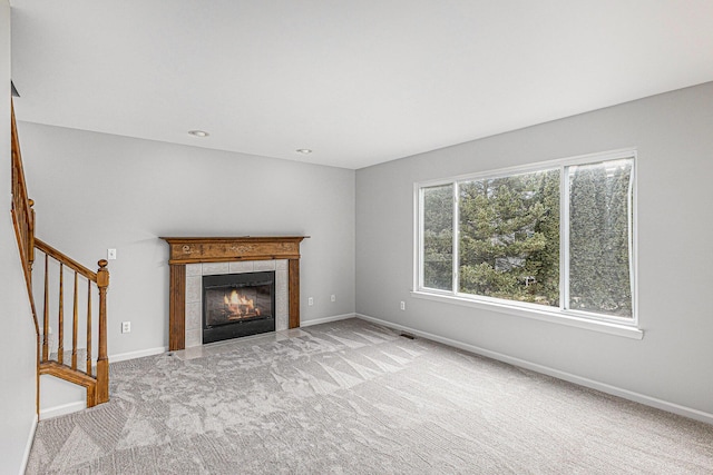 unfurnished living room featuring visible vents, a tiled fireplace, carpet floors, baseboards, and stairs