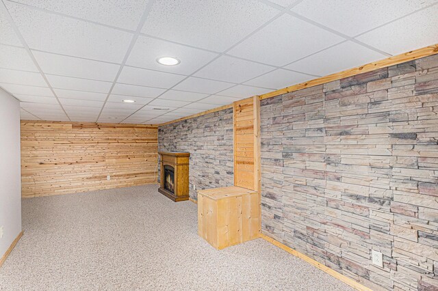 finished basement with carpet flooring, wood walls, a fireplace, and a paneled ceiling