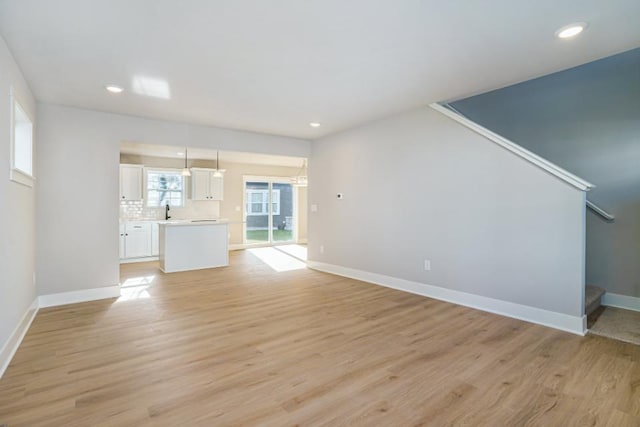 unfurnished living room featuring recessed lighting, light wood-type flooring, baseboards, and stairs