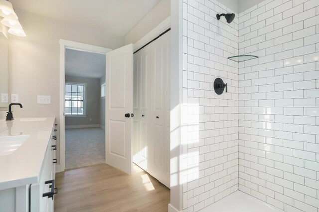 full bath featuring double vanity, wood finished floors, tiled shower, and a sink