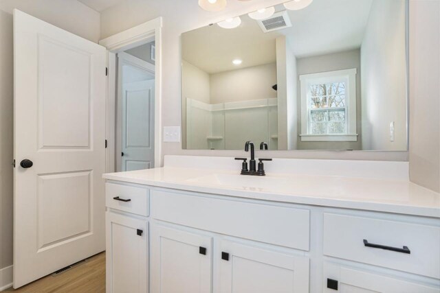 full bathroom featuring vanity, wood finished floors, a walk in shower, and visible vents