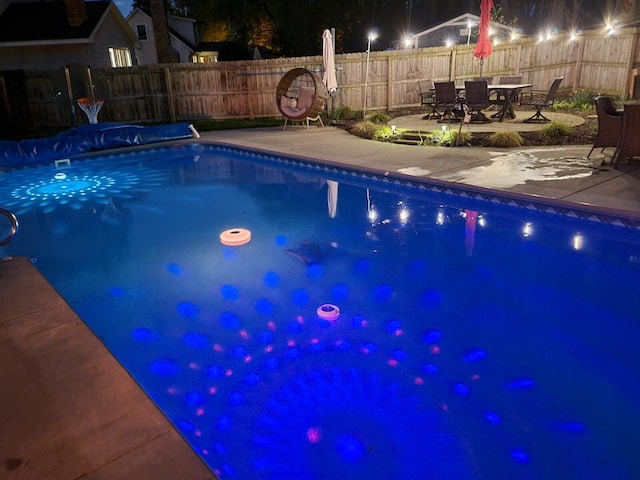 pool at night featuring a fenced backyard, a fenced in pool, and a patio