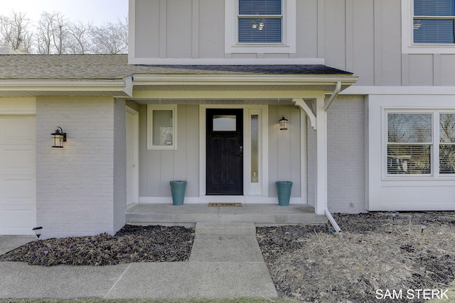 doorway to property featuring a porch, a shingled roof, a garage, board and batten siding, and brick siding