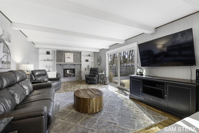 living room featuring beam ceiling, a fireplace, built in shelves, and wood finished floors