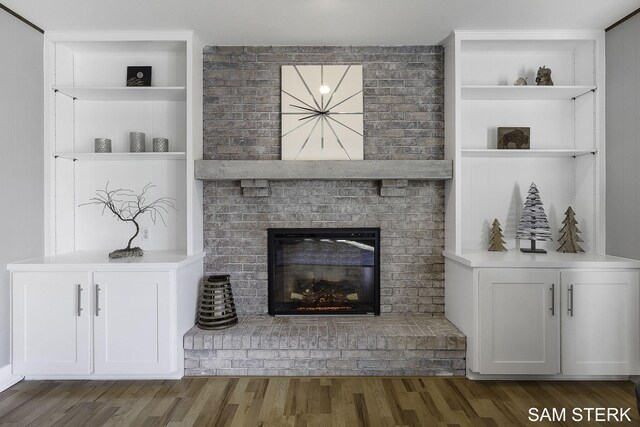 unfurnished living room featuring a brick fireplace, built in features, and wood finished floors