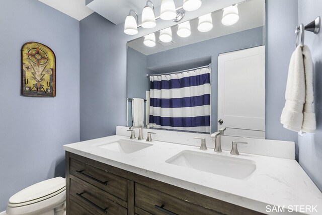 bathroom featuring a sink, toilet, a shower with shower curtain, and double vanity