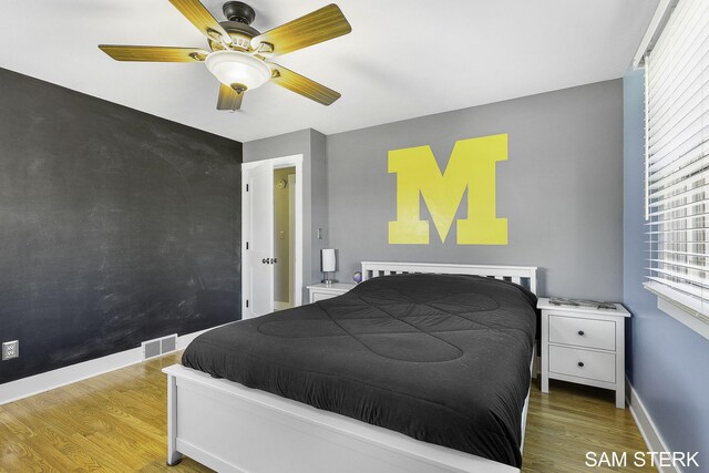 bedroom featuring visible vents, wood finished floors, baseboards, ceiling fan, and an accent wall