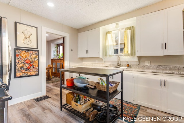 kitchen with light wood finished floors, visible vents, light countertops, white cabinets, and a sink