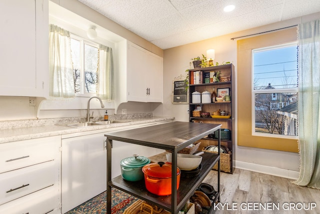 kitchen featuring a sink, light countertops, a paneled ceiling, light wood-style floors, and white cabinetry