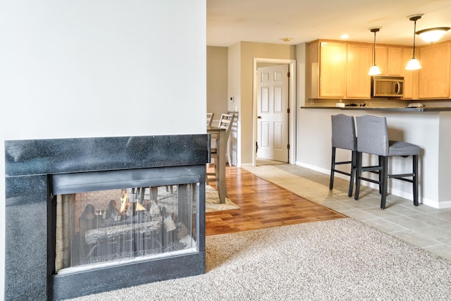 kitchen featuring stainless steel microwave, light brown cabinets, baseboards, decorative light fixtures, and light tile patterned floors