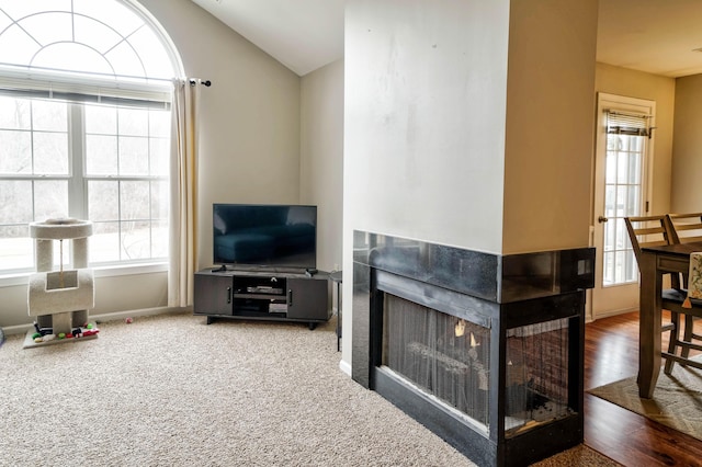 carpeted living room with a wealth of natural light, a multi sided fireplace, and vaulted ceiling