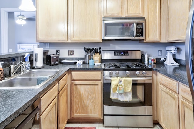 kitchen with light brown cabinets, a sink, dark countertops, stainless steel appliances, and ceiling fan