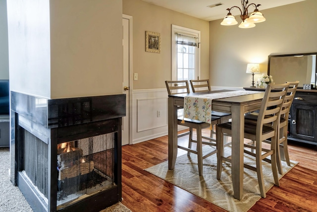 dining room with visible vents, a multi sided fireplace, a wainscoted wall, an inviting chandelier, and wood finished floors