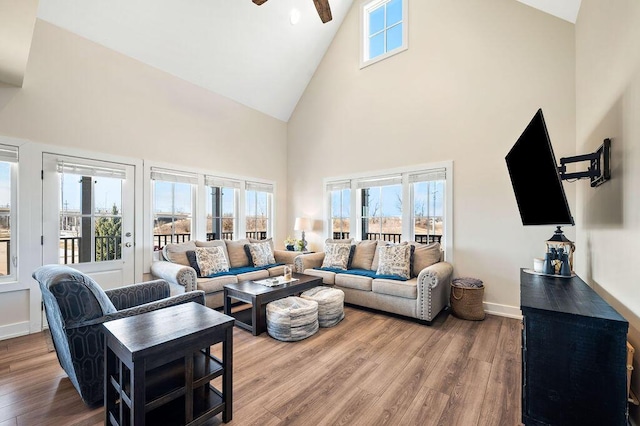 living area with ceiling fan, high vaulted ceiling, wood finished floors, and a healthy amount of sunlight