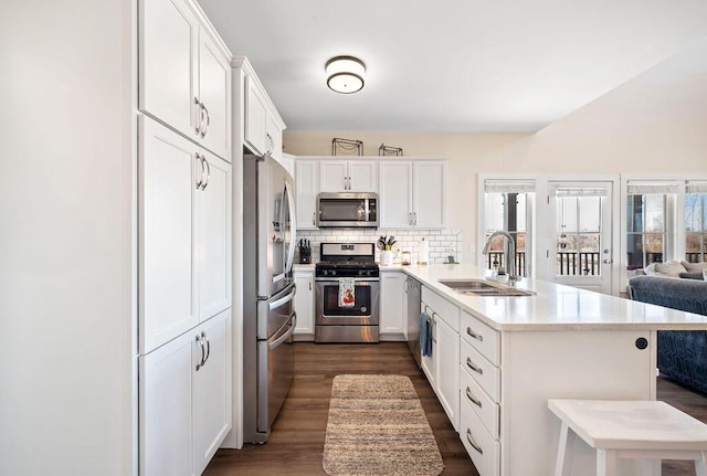 kitchen with a peninsula, a sink, decorative backsplash, light countertops, and stainless steel appliances