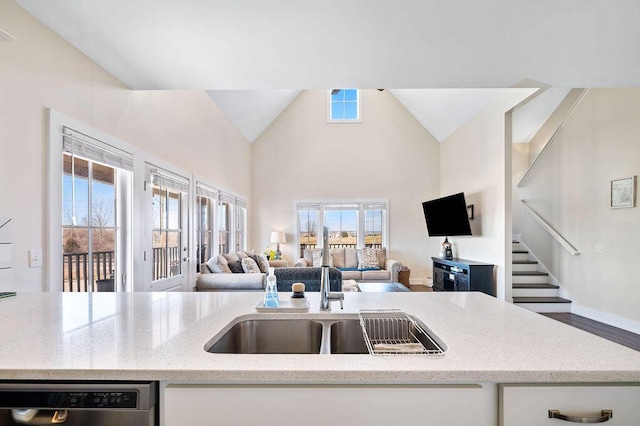 kitchen with a sink, light stone counters, stainless steel dishwasher, and open floor plan