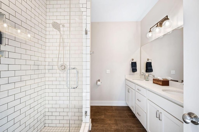 full bath with double vanity, a stall shower, baseboards, and a sink