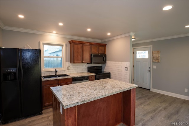 kitchen with black appliances, a sink, a kitchen island, light wood-style floors, and light countertops