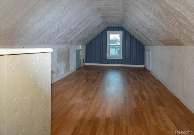 additional living space featuring vaulted ceiling, wood finished floors, baseboards, and a textured ceiling