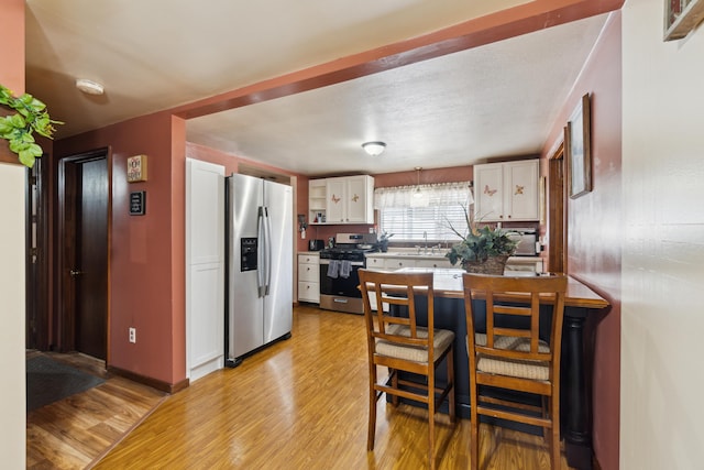 kitchen featuring a sink, white cabinetry, light wood-style floors, appliances with stainless steel finishes, and a peninsula