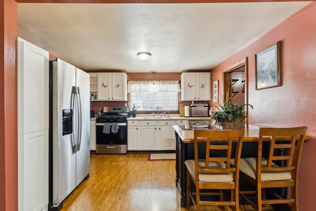 kitchen featuring light wood-style flooring, appliances with stainless steel finishes, white cabinetry, and a breakfast bar area