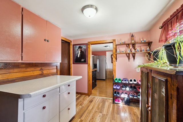 kitchen featuring light wood finished floors, open shelves, stainless steel fridge with ice dispenser, light countertops, and white cabinets