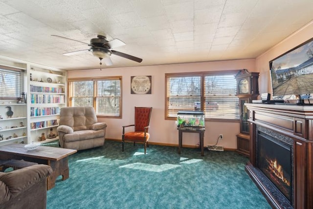 living area with baseboards, a ceiling fan, a warm lit fireplace, and carpet flooring