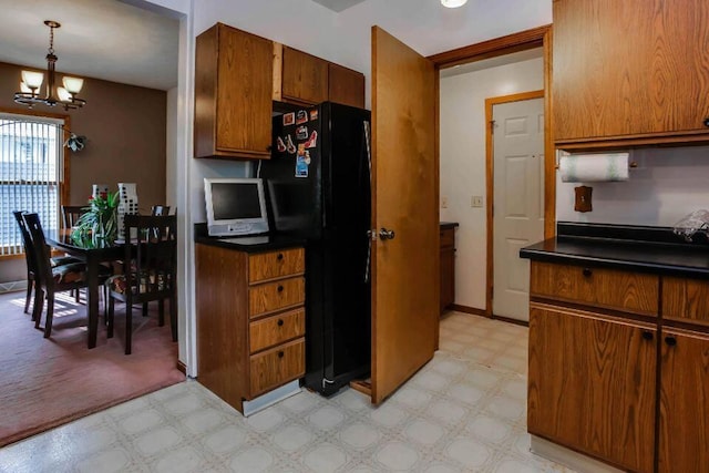 kitchen with dark countertops, light floors, freestanding refrigerator, an inviting chandelier, and brown cabinetry