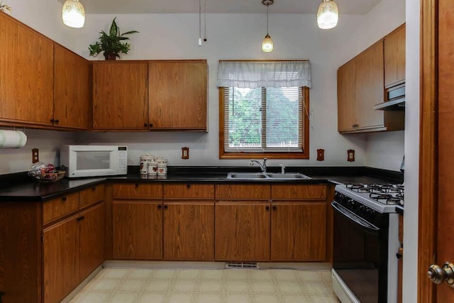 kitchen with brown cabinets, a sink, range with gas stovetop, light floors, and white microwave