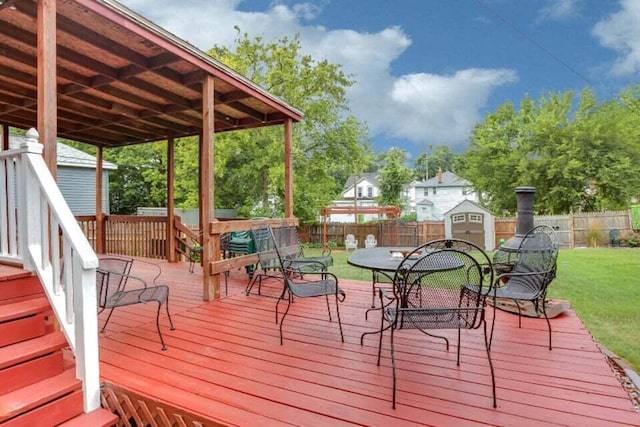 wooden terrace with a storage unit, an outbuilding, a fenced backyard, a yard, and outdoor dining area