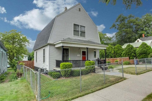 dutch colonial with a porch, a gambrel roof, a shingled roof, a front lawn, and a fenced front yard