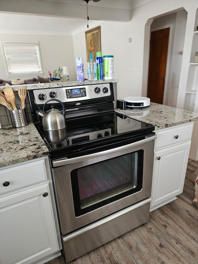 kitchen with light wood-type flooring, electric range, light stone countertops, and white cabinetry