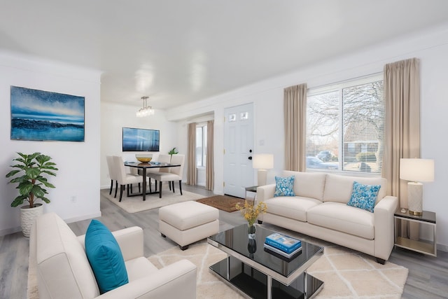 living area featuring baseboards, plenty of natural light, a notable chandelier, and light wood finished floors