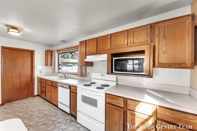 kitchen featuring under cabinet range hood, light floors, light countertops, white appliances, and a sink