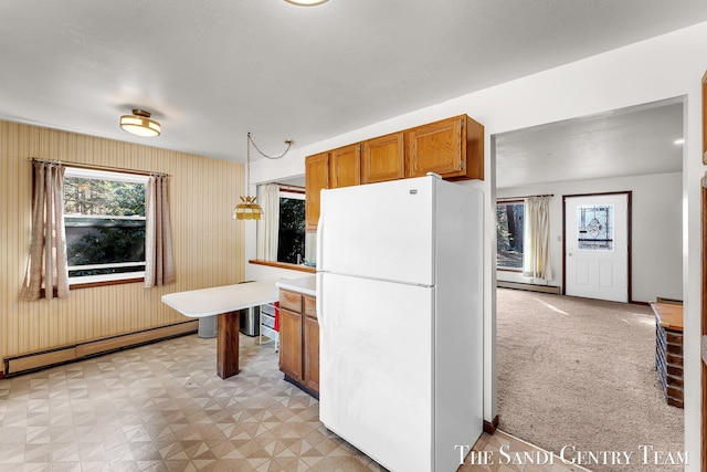 kitchen with brown cabinets, freestanding refrigerator, light countertops, baseboard heating, and hanging light fixtures