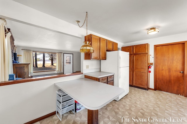 kitchen with baseboards, light floors, light countertops, freestanding refrigerator, and brown cabinetry