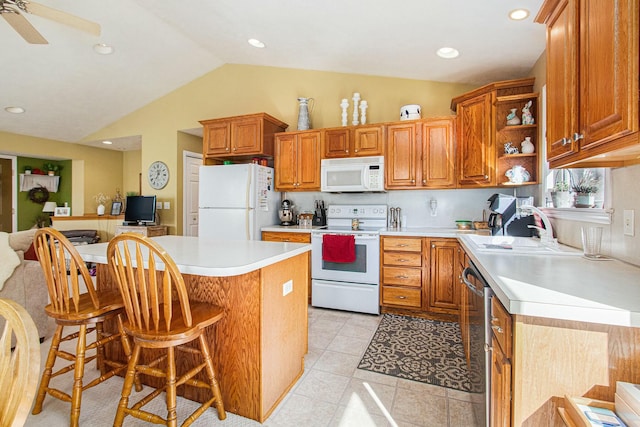 kitchen featuring white appliances, brown cabinetry, a sink, light countertops, and a kitchen bar