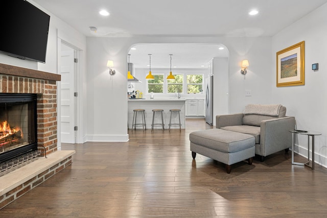 living room with recessed lighting, baseboards, a brick fireplace, and wood finished floors