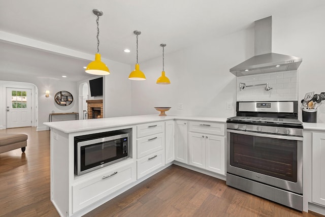 kitchen with dark wood finished floors, a peninsula, light countertops, appliances with stainless steel finishes, and wall chimney exhaust hood