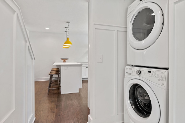 laundry area featuring laundry area, dark wood-style flooring, stacked washer / drying machine, wainscoting, and a decorative wall